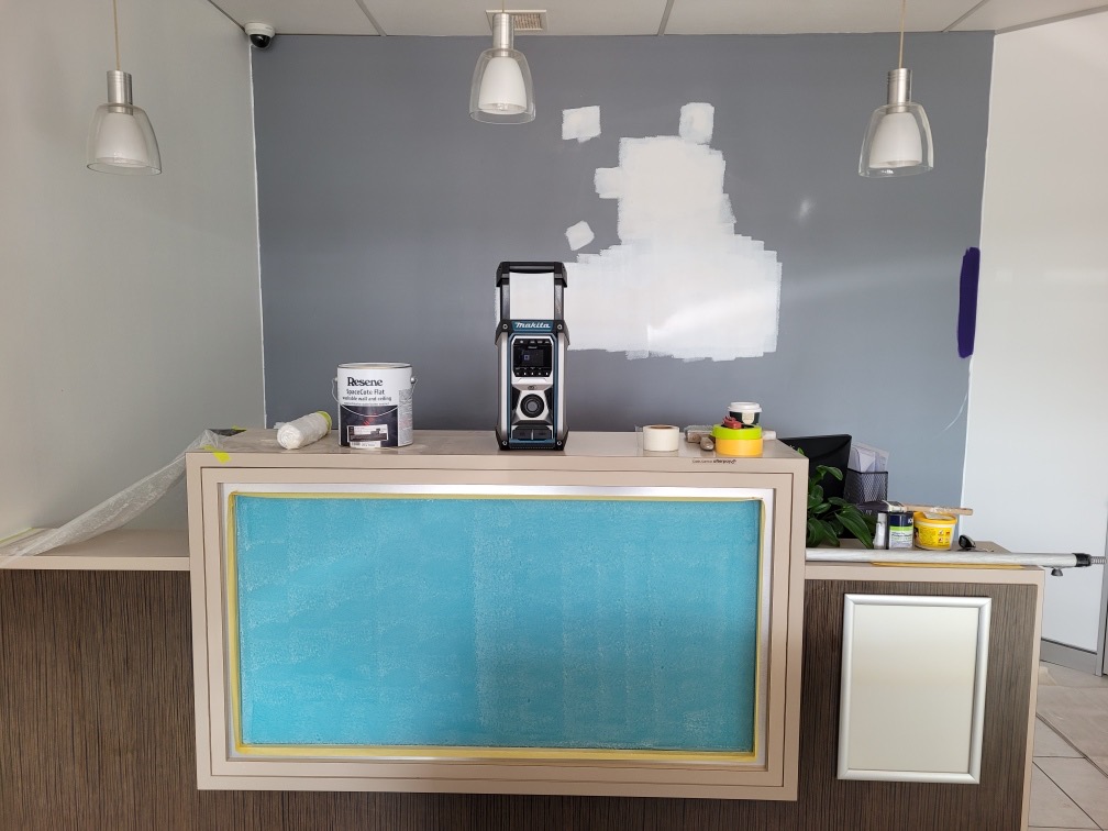 Reception desk area mid-renovation with grey wall being prepped and paint supplies