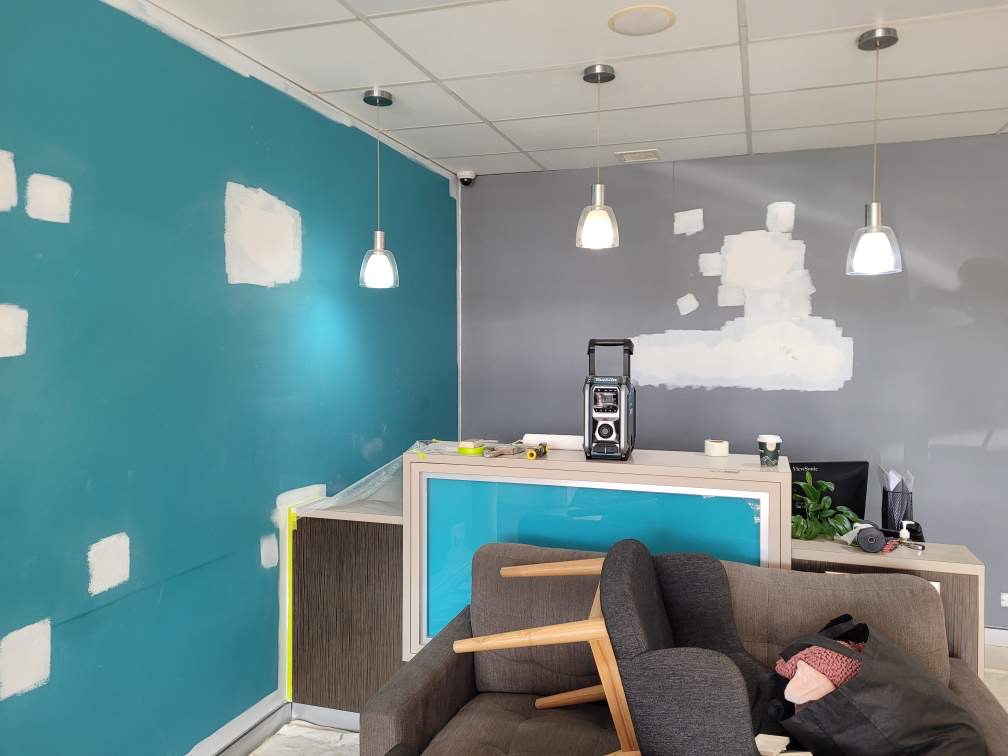 Reception mid-paint — teal wall with primer patches and Resene paint cans during renovation